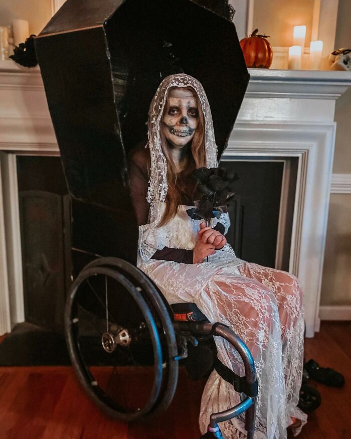 A person with skeleton face paint in a wheelchair designed like a black coffin for Halloween.