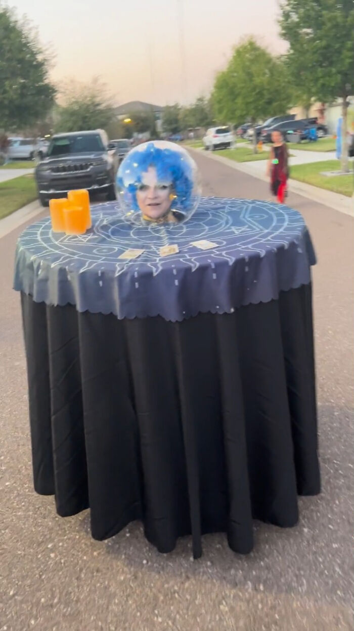 Woman sitting inside a fortune teller table costume made for creative people with disabilities on Halloween.
