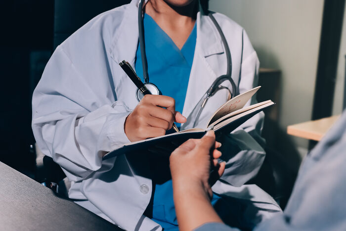 Close-up of a doctor writing on a notepad, discussing rising Gen Z health problems with a patient.