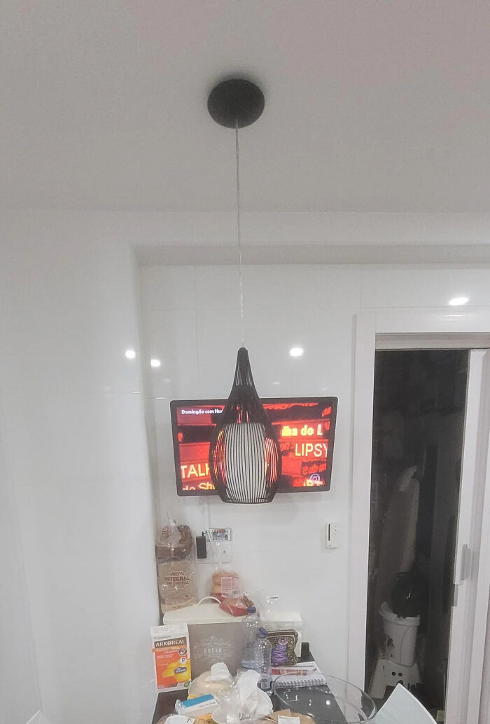 A modern black pendant light hanging unevenly in front of a wall-mounted TV during a home renovate attempt