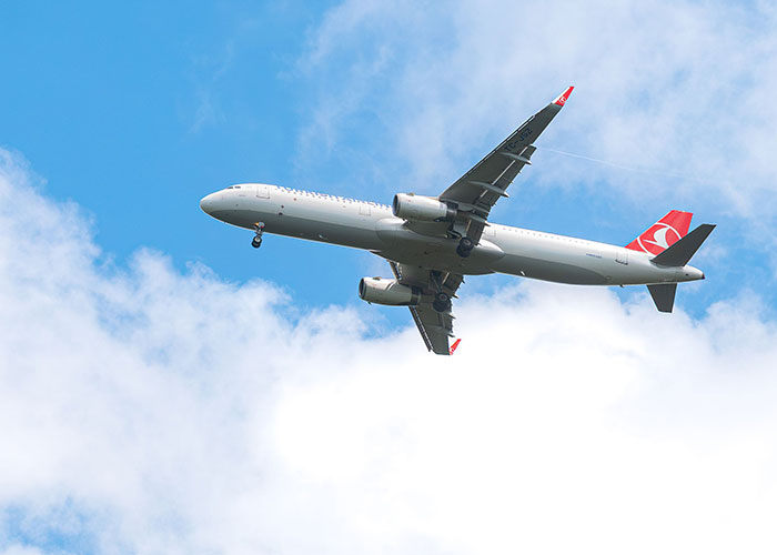 Commercial airplane flying high in blue sky with clouds