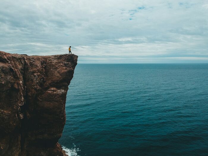 A person standing on the edge of a high cliff looking over the ocean, reminiscent of a dramatic Hollywood scene.