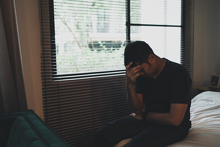 A thoughtful man sitting on a bed reflecting after his parents dismiss son’s achievements for years. A thoughtful man sitting on a bed reflecting after his parents dismiss son’s achievements for years.