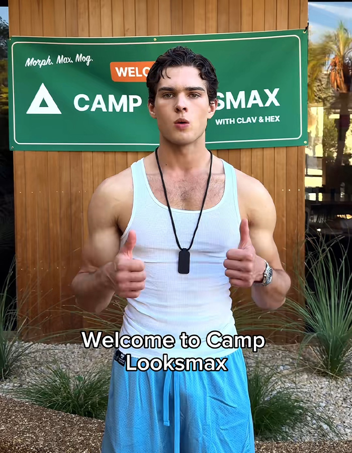A young athletic man giving two thumbs up in front of a banner at a looksmaxxing camp. A young athletic man giving two thumbs up in front of a banner at a looksmaxxing camp.