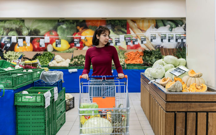 A woman stands with a shopping cart in a supermarket, referencing forgets to pay at checkout. A woman stands with a shopping cart in a supermarket, referencing forgets to pay at checkout.
