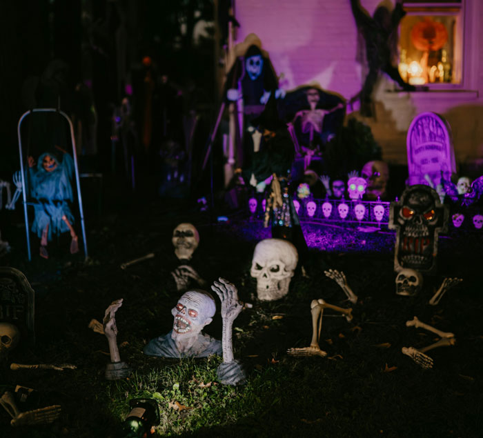 Spooky Halloween yard decorations illuminated at night for a neighbor paid tour concept.