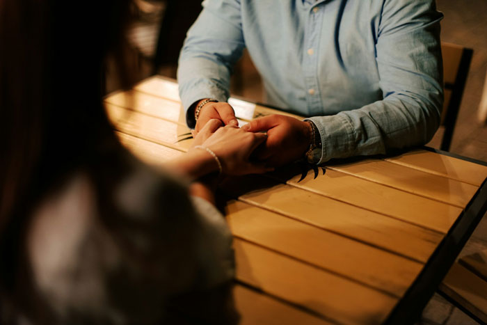Couple holding hands sitting at a wooden table symbolizing engagement conversations Couple holding hands sitting at a wooden table symbolizing engagement conversations