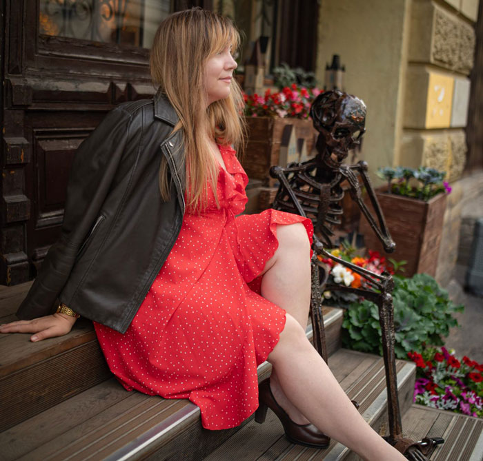 Woman in red dress sitting on steps next to a skeleton decoration, representing a paid tour tourist.