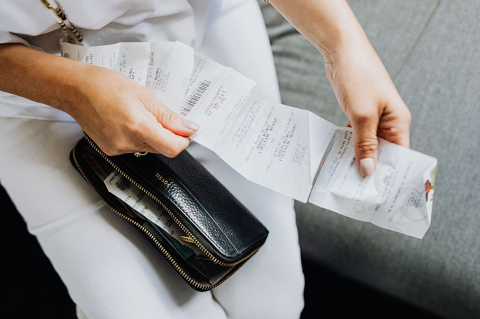 Woman holding a long checkout receipt in her hands with her wallet open. Woman holding a long checkout receipt in her hands with her wallet open.