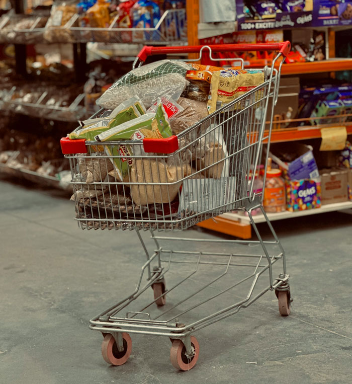 A shopping cart overflowing with grocery items inside a supermarket. A shopping cart overflowing with grocery items inside a supermarket.