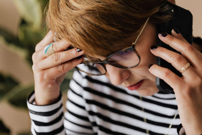 A worried woman holding her head while on the phone, illustrating a mom losing sleep over family drama. A worried woman holding her head while on the phone, illustrating a mom losing sleep over family drama.