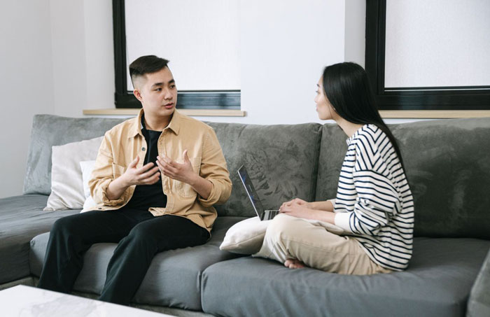 Couple discussing engagement plans on a gray couch Couple discussing engagement plans on a gray couch