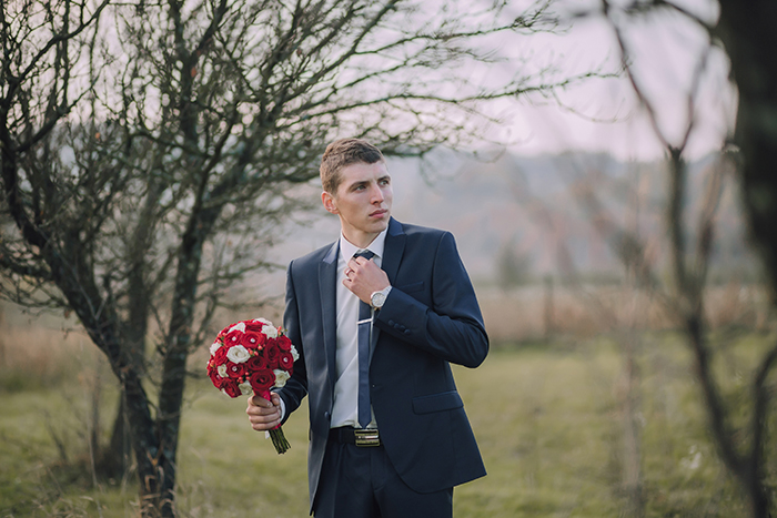 A man in a suit holding flowers for a dream proposal outside.