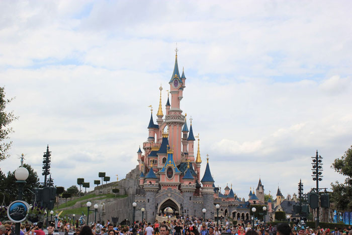 A wide shot of the iconic Disneyland castle under a cloudy sky during a family trip. A wide shot of the iconic Disneyland castle under a cloudy sky during a family trip.