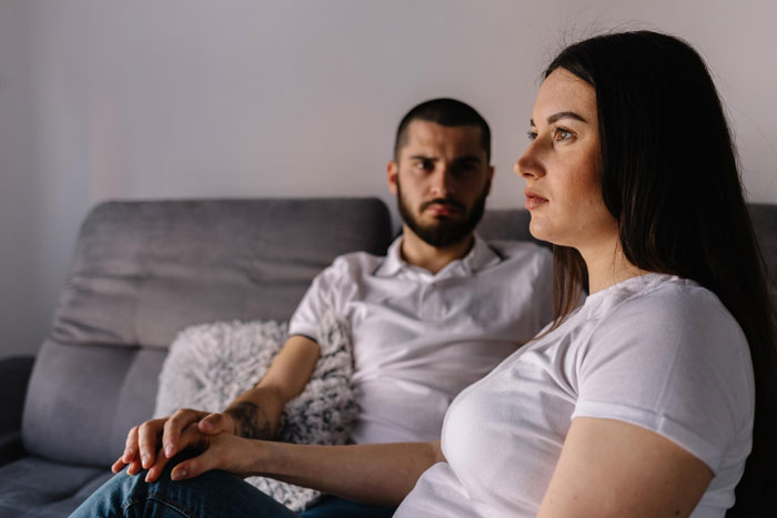 A worried man sitting on a couch next to a woman during a tense moment of family drama A worried man sitting on a couch next to a woman during a tense moment of family drama