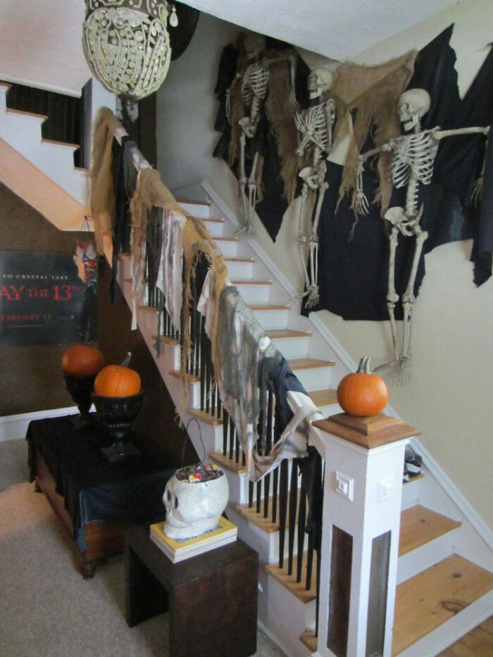 Indoor staircase decorated with hanging skeletons, pumpkins, and spooky fabric for Halloween.