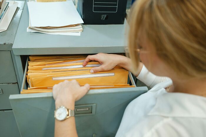 Office worker searching through file folders in a metal cabinet, showing behind the scenes document management