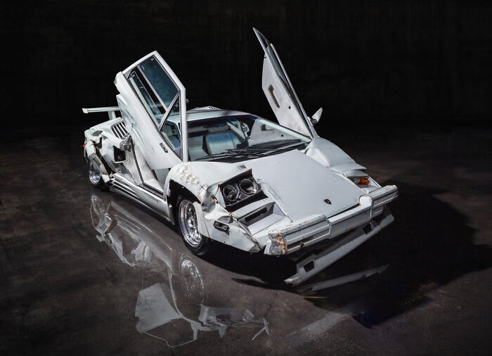 A damaged white Lamborghini Countach used as movie props on a dark showroom floor.