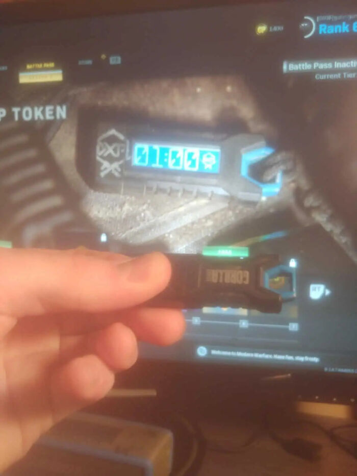 Hand holding a small black electronic device next to a monitor, showcasing cool movie props.