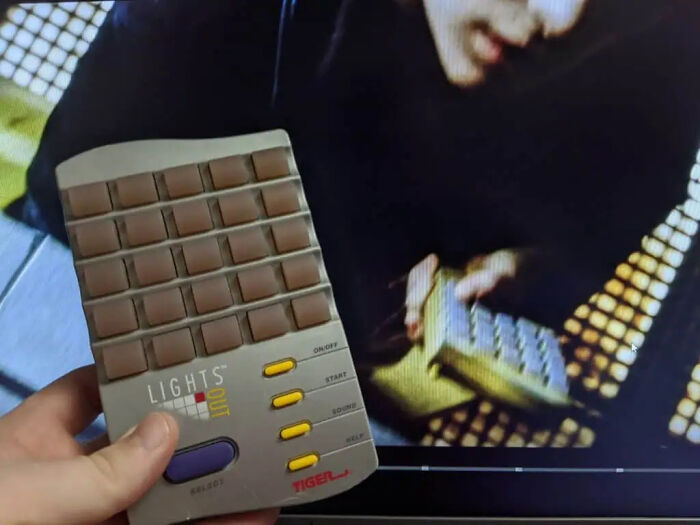 A hand holding a vintage Tiger Lights Out electronic game utilized as movie props.