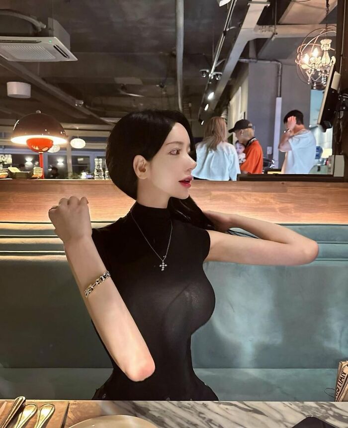 Ridiculously edited woman with elongated arms and neck sitting in a restaurant
