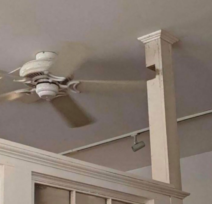 A white ceiling fan with a blade going through a cutout in a pillar, showing bad home renovation choices.
