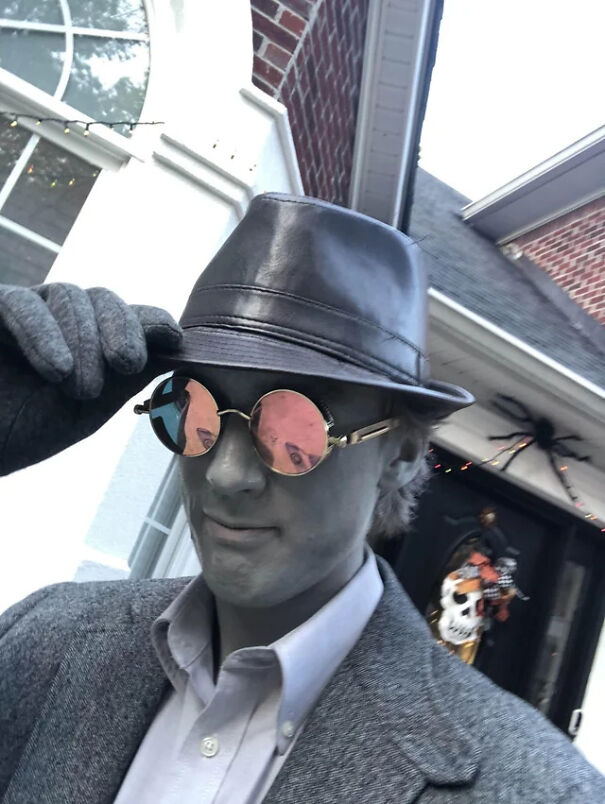 A man in grey makeup, hat, and sunglasses posing as a black and white film character for Halloween costume ideas.