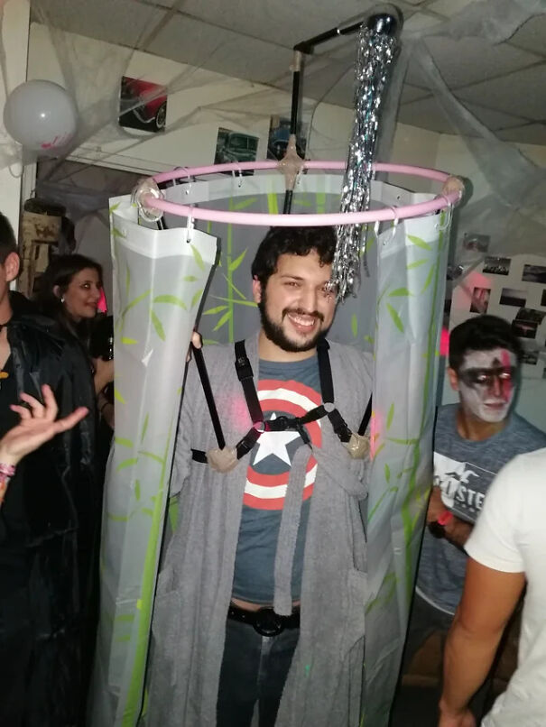 A man wearing a homemade shower stall contraption as a unique Halloween costume idea at a party.