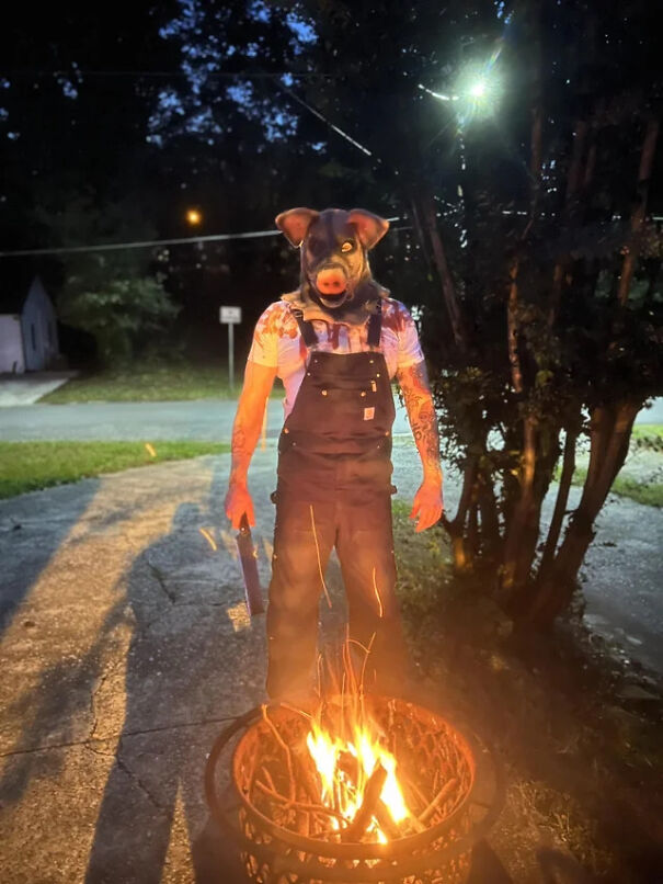 Person in a scary pig mask and overalls standing by a fire, showing creepy Halloween costume ideas.