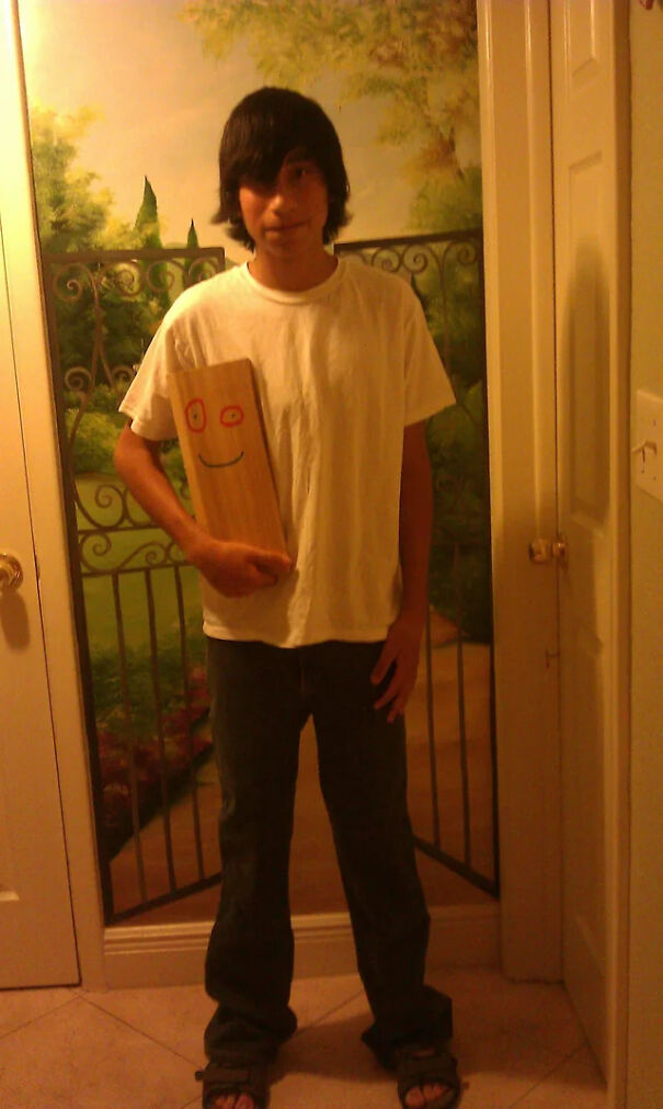 A young man holding a wooden plank with a face drawn on it for a quick Halloween costume idea.
