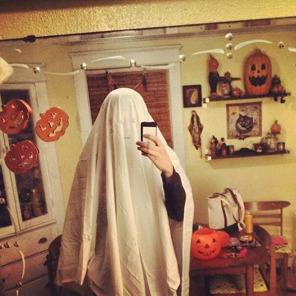 Person taking a mirror selfie dressed as a classic ghost sheet, a last-minute cool Halloween costume idea.