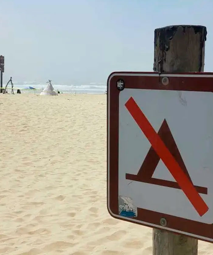 A sign prohibiting tents on a beach with an actual tent visible in the background