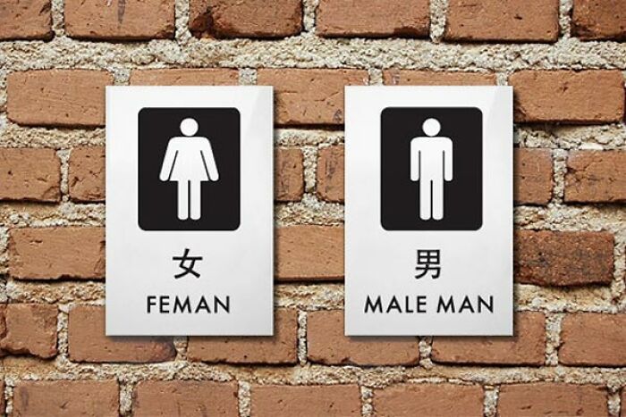 Restroom signs showing translation fails with FEMAN and MALE MAN written on a brick wall.