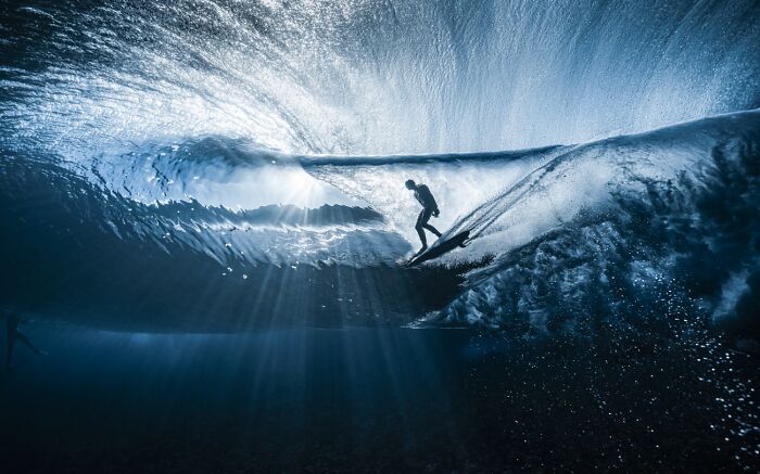Surfer riding wave underwater with light beams shining through, best pics 2026 Siena International Photo Awards