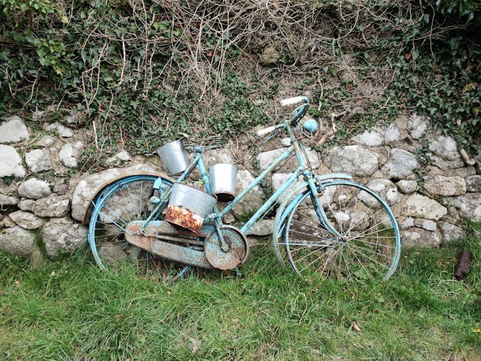 Rustic blue bicycle with metal buckets leaning against a stone wall, a unique dumpster find.