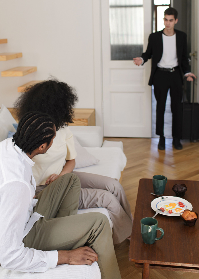 Unannounced guest arriving with luggage at friends apartment, illustrating couch surfing debate Unannounced guest arriving with luggage at friends apartment, illustrating couch surfing debate