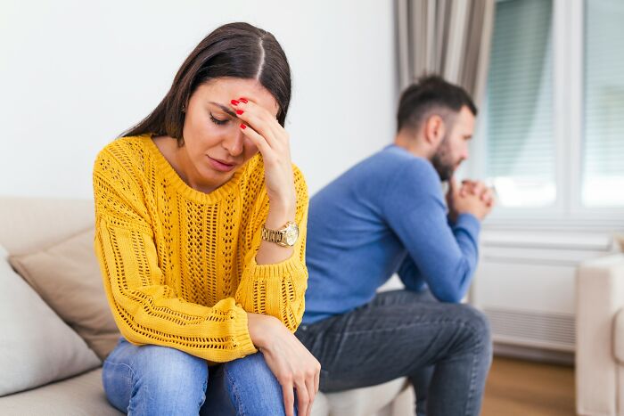 An upset woman sitting on a couch with a distant partner, reflecting emotional infidelity stories.