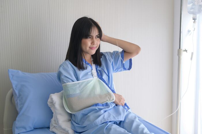 A female patient with an arm sling sitting in a hospital bed after professionals made clients lose trust