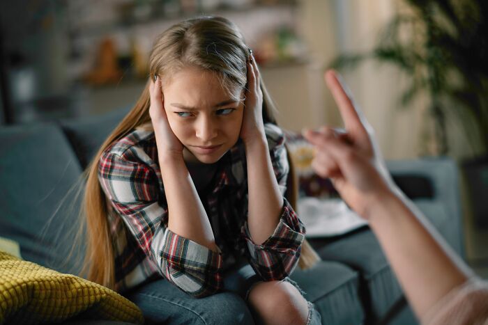 A young woman covering her ears while someone scolds her, showing toxic behavior from narcissistic parents.