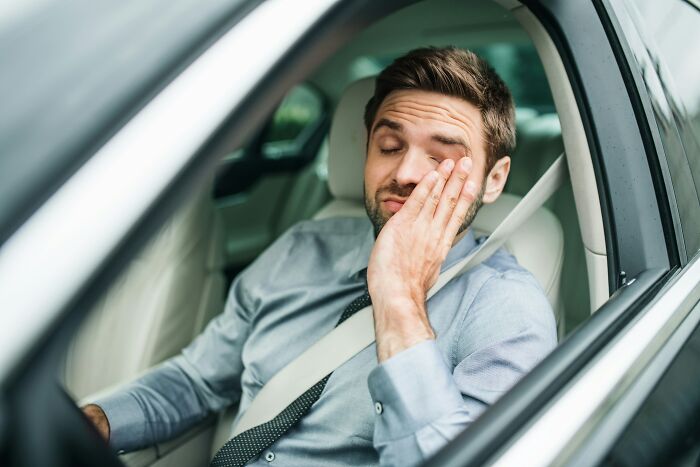 Tired driver rubbing eye inside car wearing seatbelt