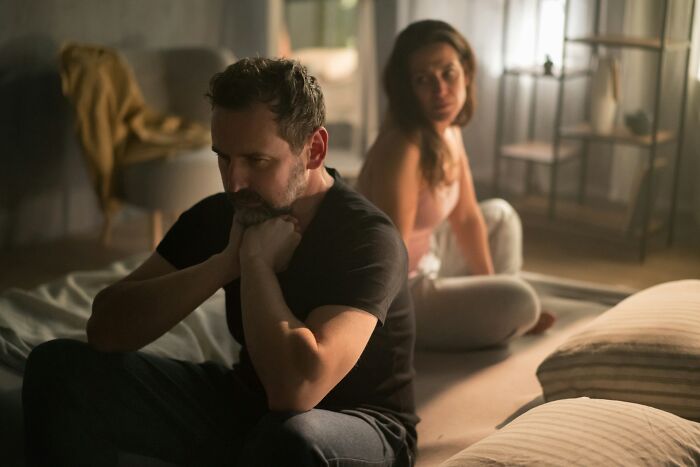 Sad couple sitting in a dim room after painful infidelity stories unfold in their relationship.