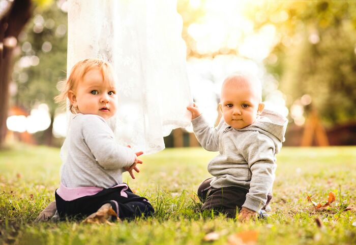 Two young toddlers sitting outdoors on grass, representing complex family dynamics in infidelity stories.