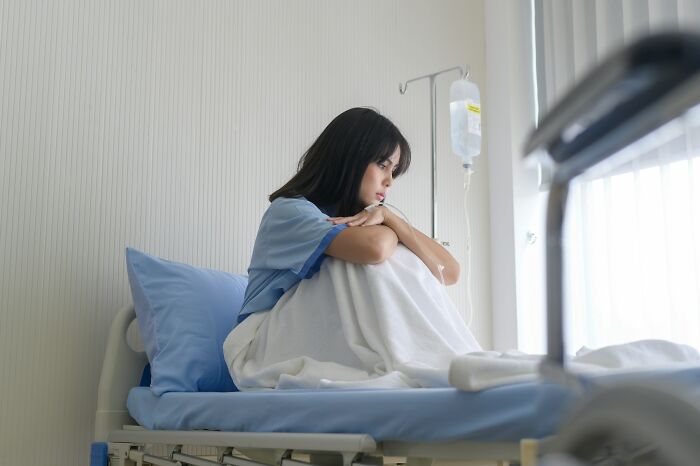 Sad woman sitting on hospital bed looking out window