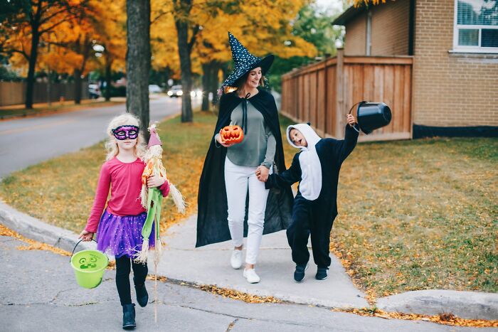 Family in Halloween costumes walking together while trick-or-treating in the neighborhood