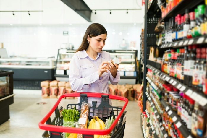 A woman checking a food jar label in a grocery store, representing fights over olive oil and cashews A woman checking a food jar label in a grocery store, representing fights over olive oil and cashews