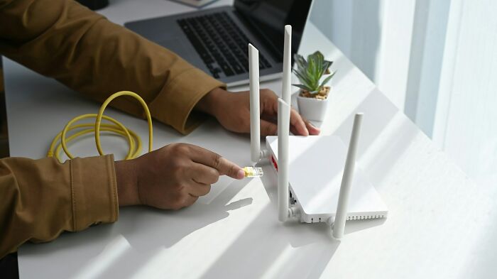 A person plugging an ethernet cable into a Wi-Fi router illustrating clever life tricks for tech setup