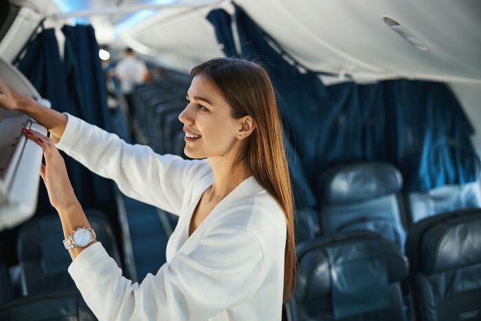 A woman smiles while placing her hand luggage into the overhead bin on flights
