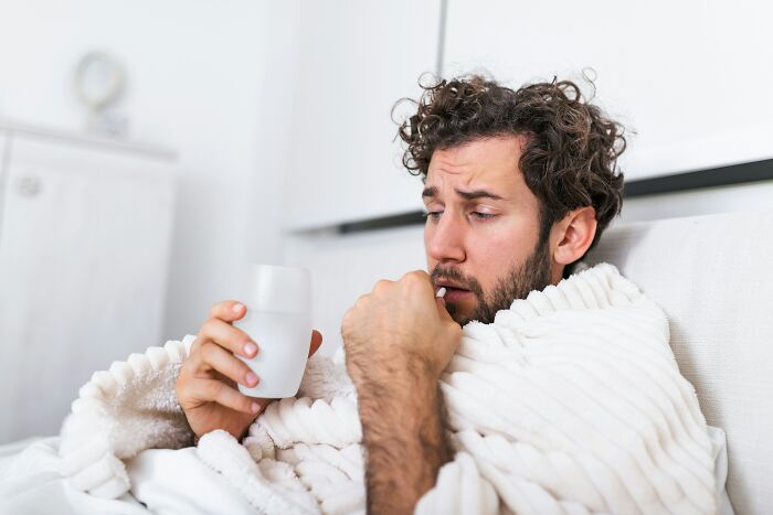 A man under a blanket taking a pill, showing moments that make partners question their intelligence.