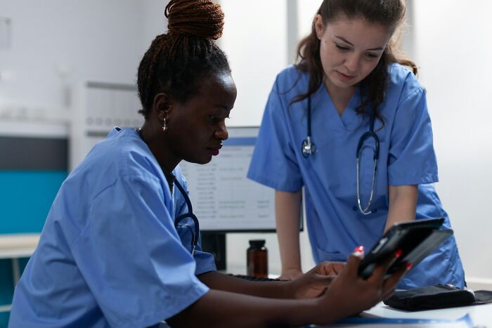 Two medical nurses reviewing a digital tablet, tied to shocking real infidelity stories.