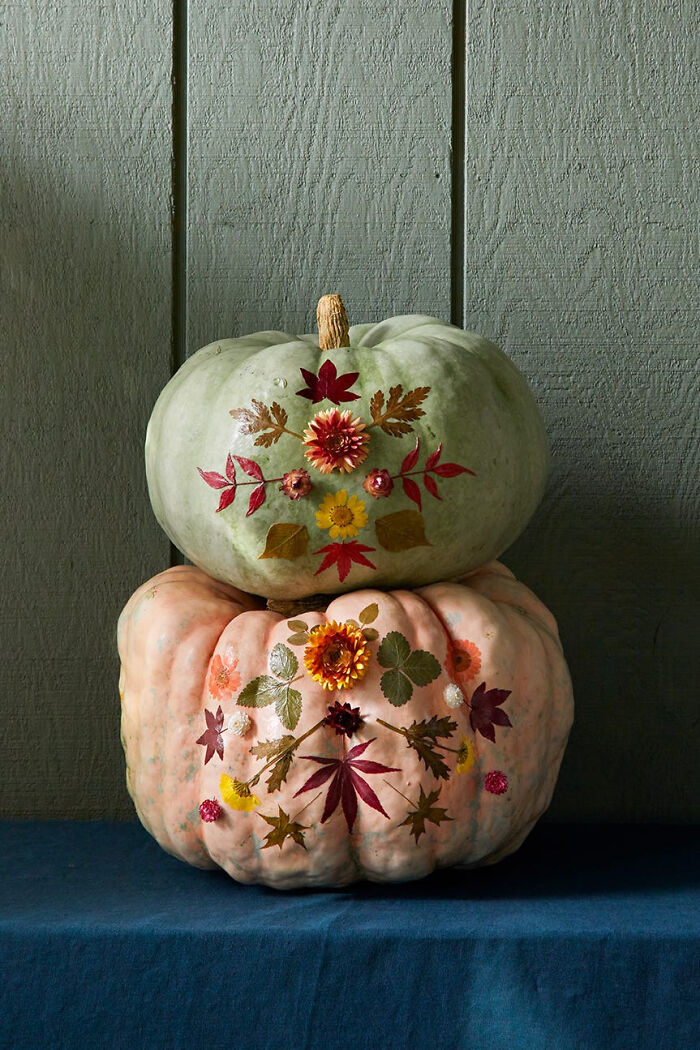 Two stacked pumpkins decorated with pressed flowers and leaves for creative Halloween decor.
